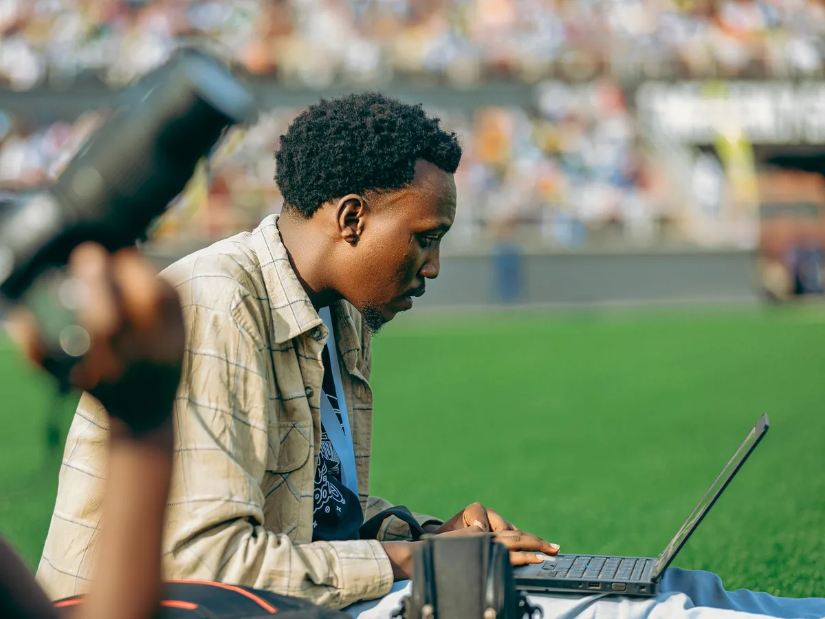 A man working on a laptop at the side of a football pitch