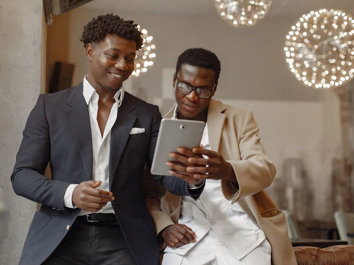 Two men in jackets smiling as they look at a tablet together