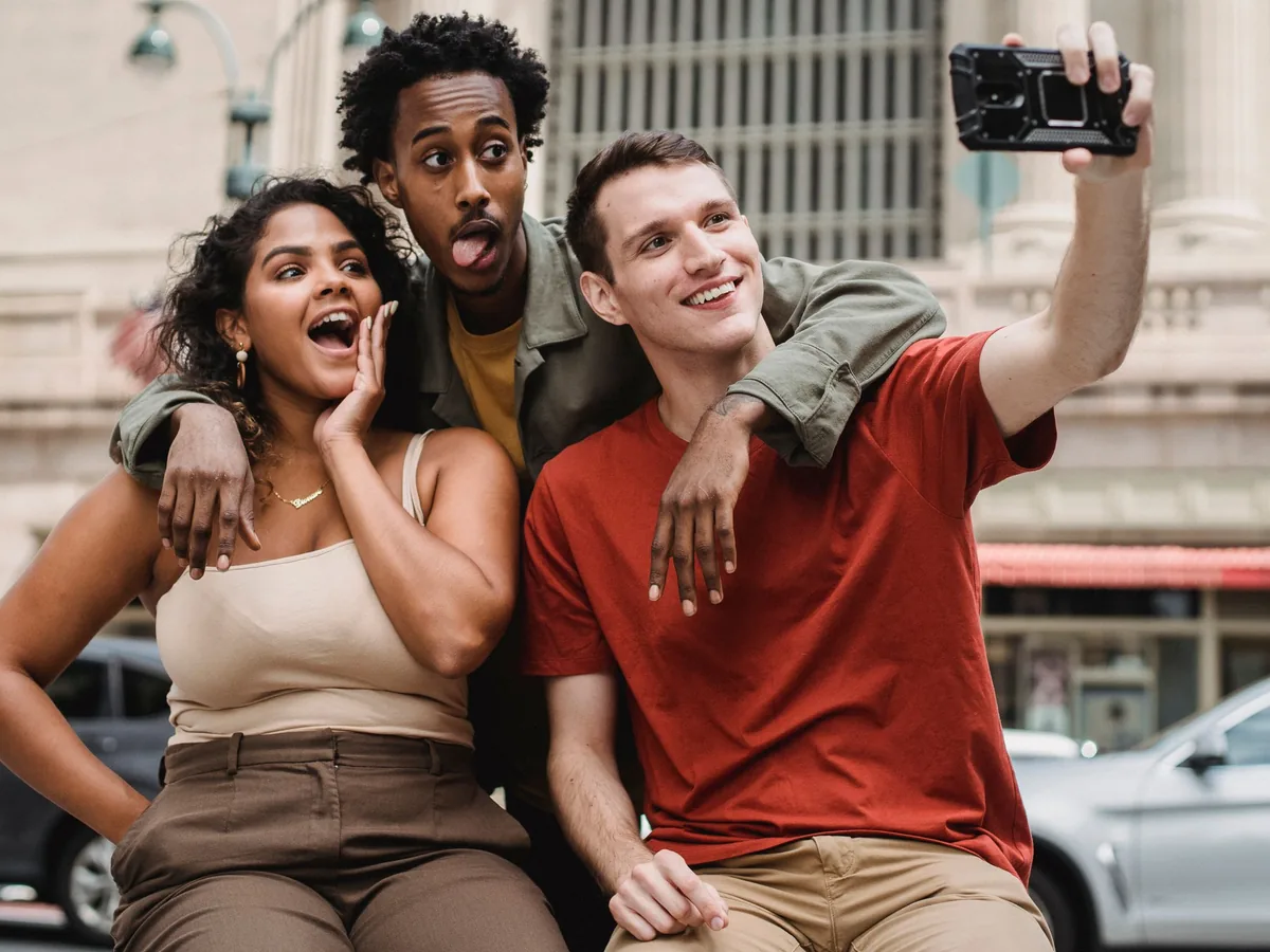 Three friends smiling and pulling faces as they take a selfie on a city street